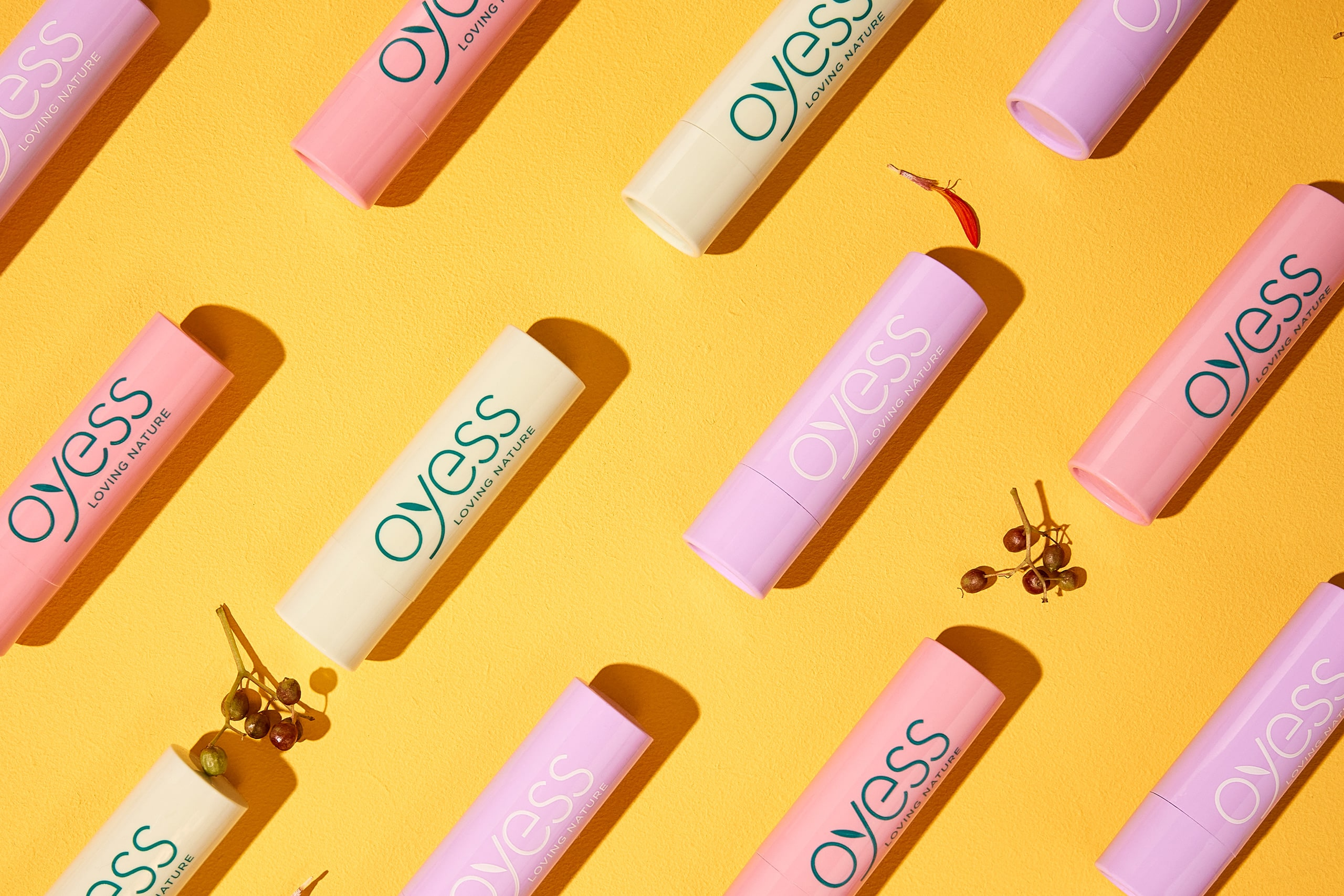 Several sticks of OYESS lip balm on a yellow coloured surface.