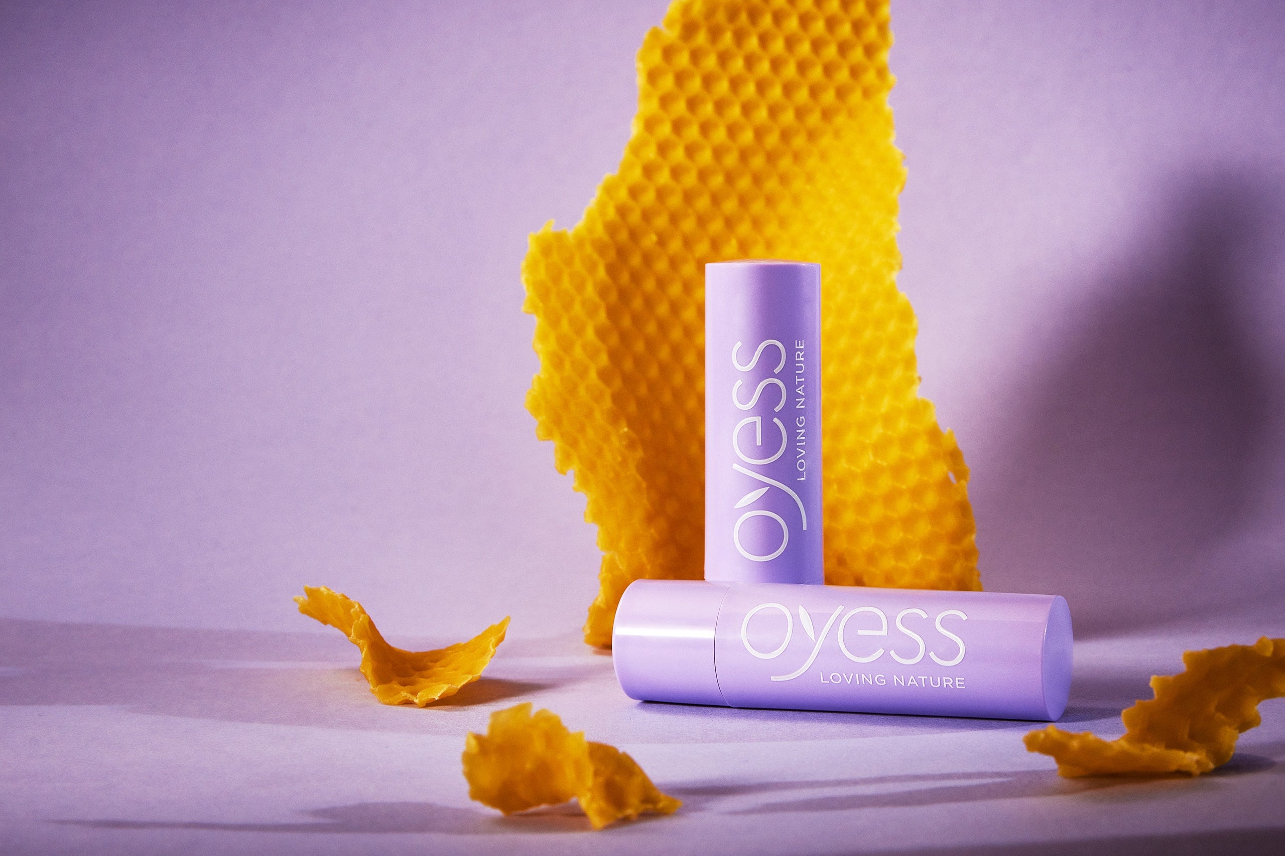 2 Extra Care Lippenbalsams vor lila Hintergrund mit eine paar Streifen gelbem Honigwachs